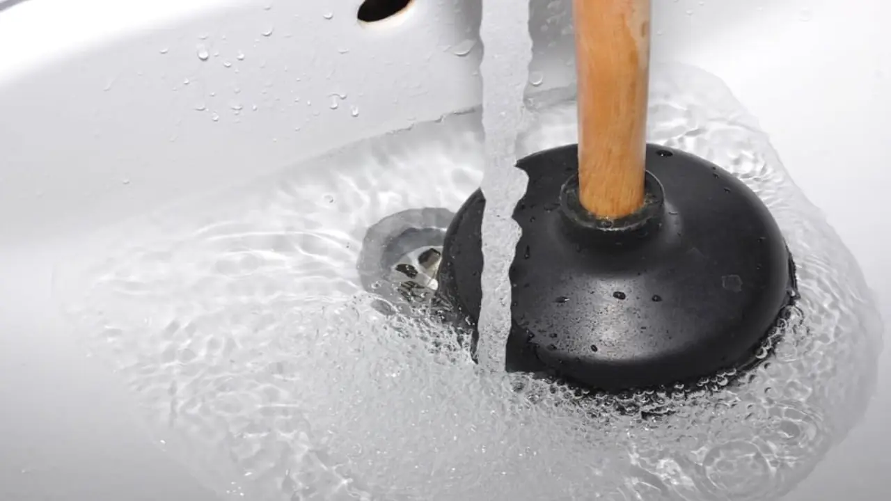 Plunger beside a sink drain with standing water